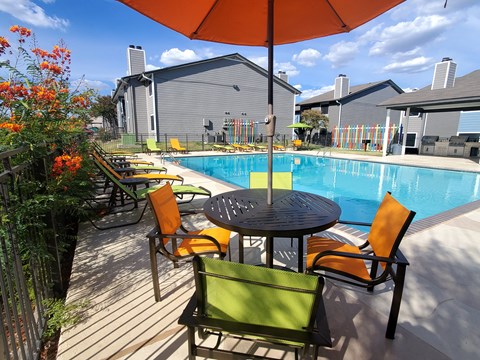 A table with chairs and an umbrella is in front of a pool.