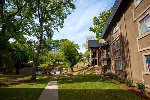 A tree-lined walkway leads to a building with a balcony.