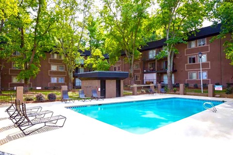 A swimming pool surrounded by trees and chairs in front of apartment buildings.