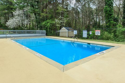A blue swimming pool surrounded by a fence and trees.