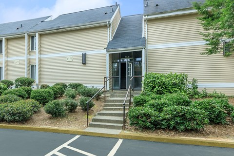 A building with a beige facade and a black roof with a set of stairs leading up to the entrance.