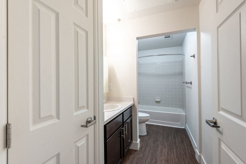 Bathroom with bathtub style shower, toilet, sink, and dark brown cabinets and grey counter top