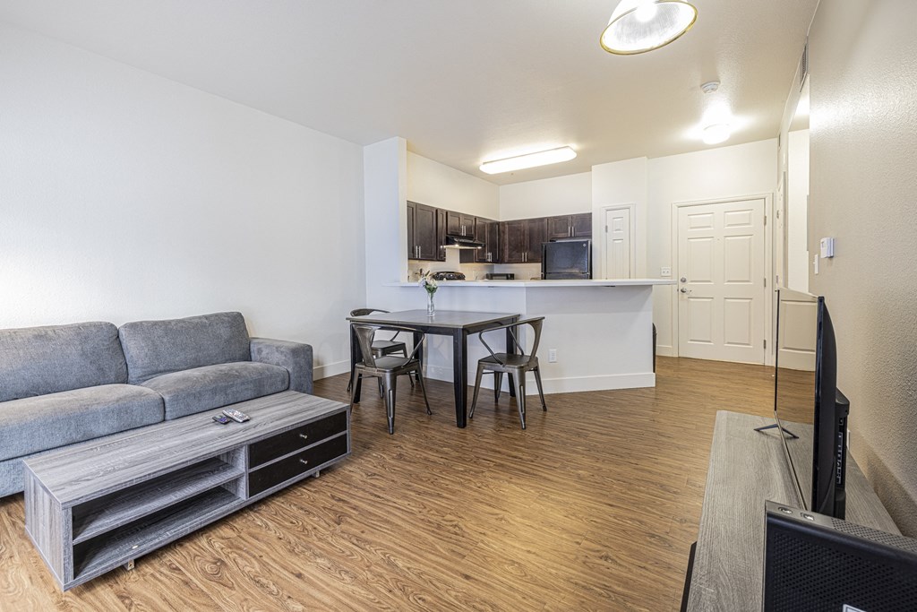 A living room with a couch, coffee table, dinette, tv on an entertainment staff, with a view of the kitchen