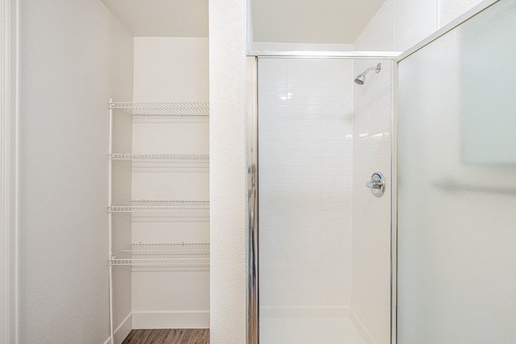 A shower stall next to an open storage area with open shelving