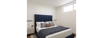 A bed with a dark blue headboard and a white mattress is in a room with white walls.