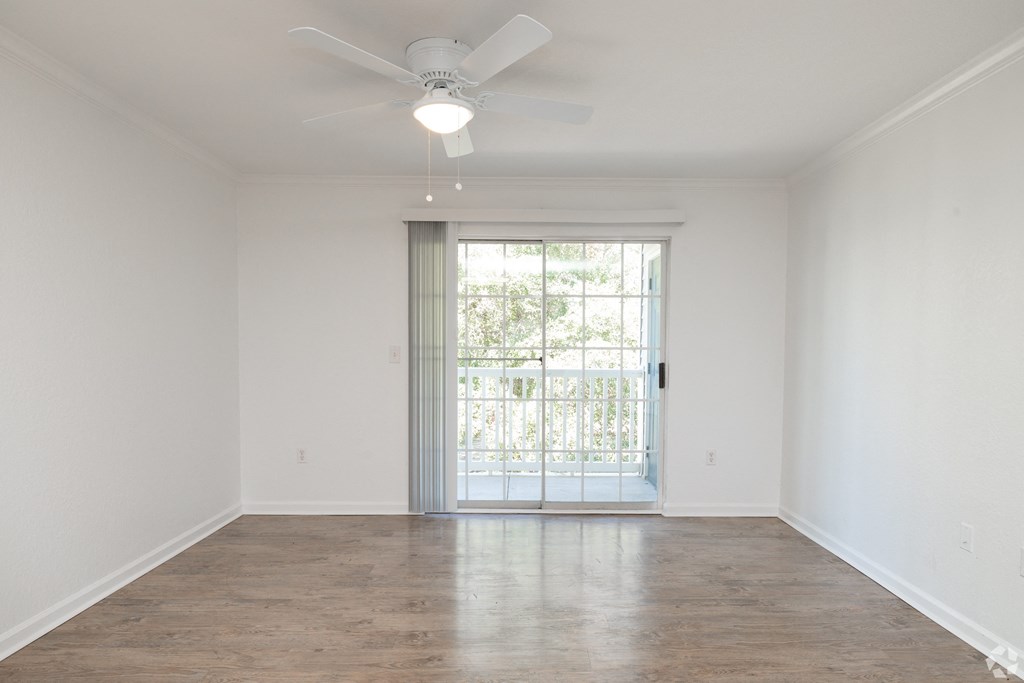 A room with a ceiling fan and sliding glass doors leading to a balcony.