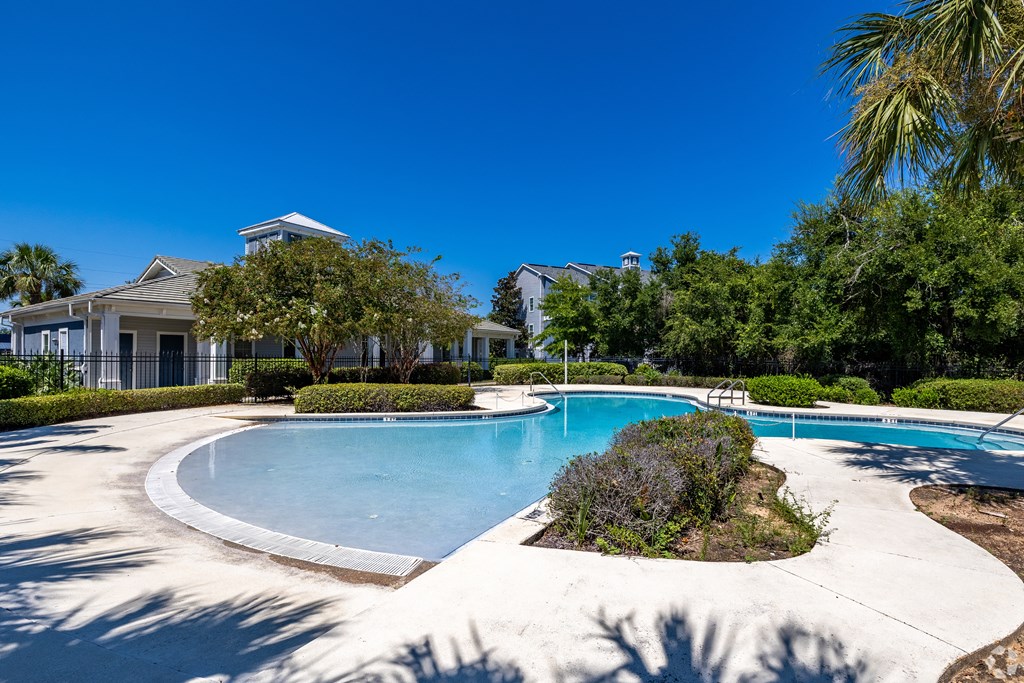 A swimming pool surrounded by a white fence and green trees.