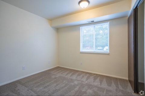 A room with a carpeted floor and a window with blinds.