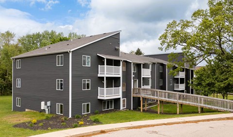 A grey apartment building with a balcony and a small garden in front.