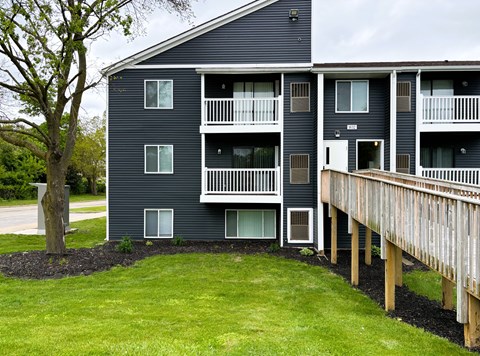 A large apartment building with a balcony and a tree in front.