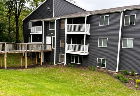 A grey building with white balconies and a green lawn in front.