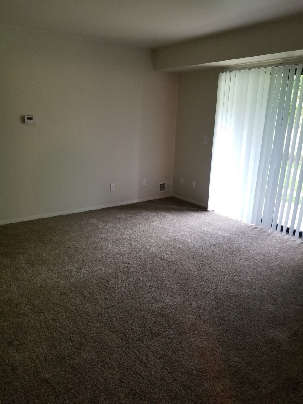 an empty living room with a large window and carpeting
