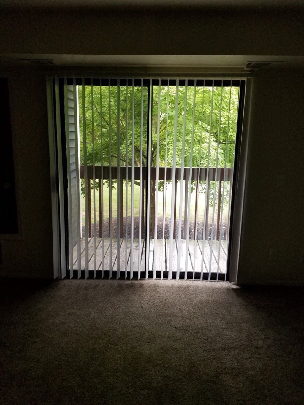 a room with blinds on a window with trees in the background