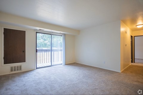 A room with a carpeted floor, a window with blinds, and a sliding glass door leading to a balcony.