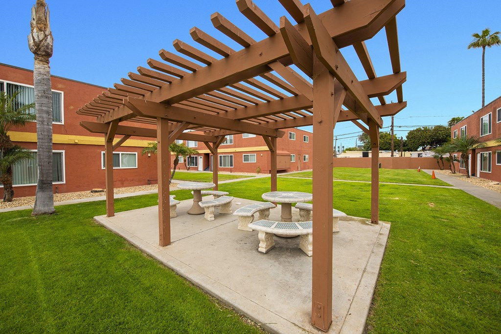a picnic area with benches and a pergola in front of a building at Casa Victoria Apartments, Chula Vista, CA
