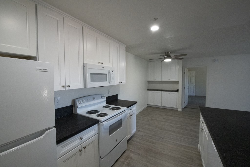an empty kitchen with white appliances and white cabinets at Sycamore Hills Village Apartments, California