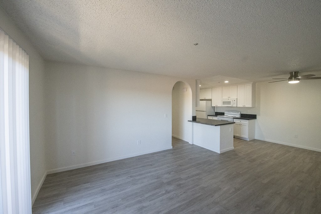an empty living room and kitchen with white walls and wood flooring at Sycamore Hills Village Apartments, California