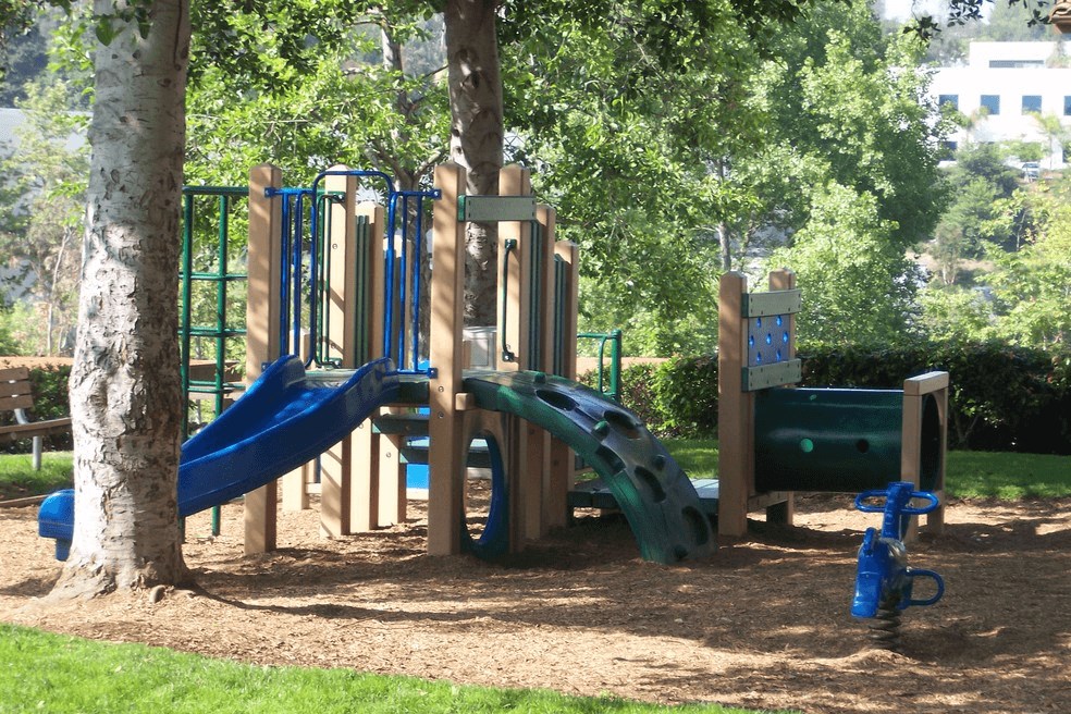 a playground with slides and trees in a park at Sycamore Hills Village Apartments, Vista, California