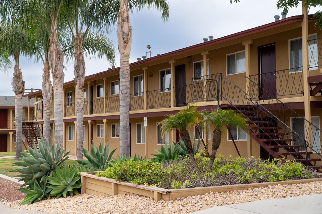 a building with palm trees and plants in front of it at Villa Primavera Apartments, National City, CA 91950