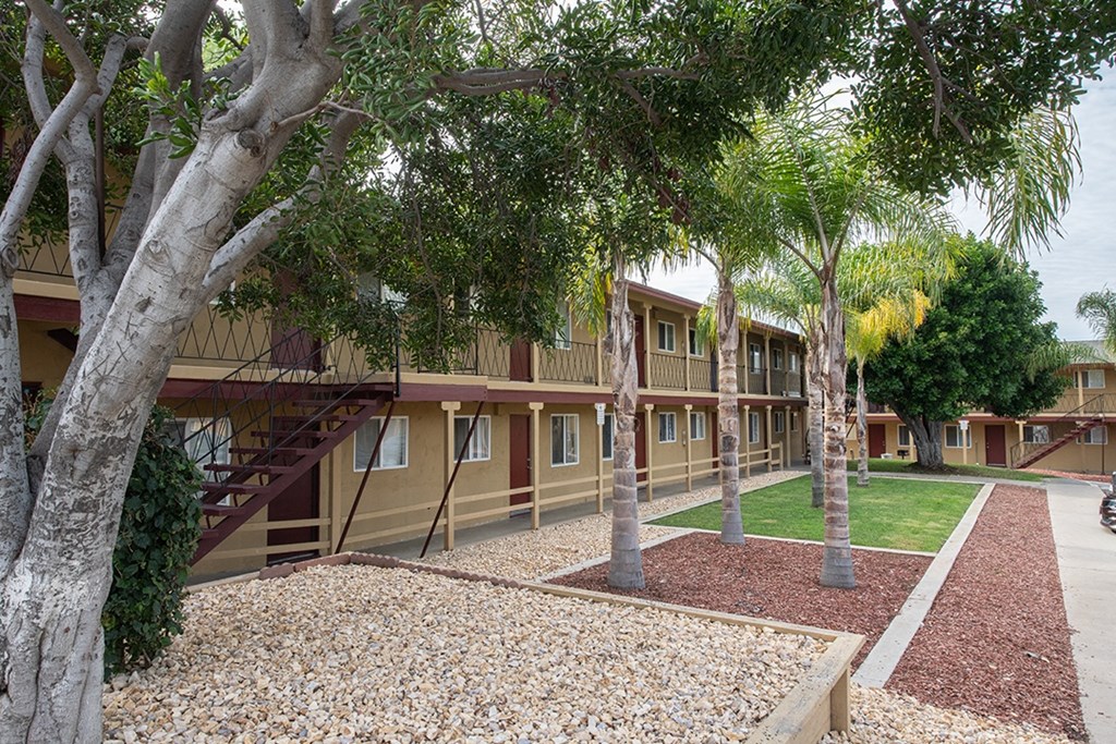 an exterior view of a building with trees and gravel at Villa Primavera Apartments, National City, 91950