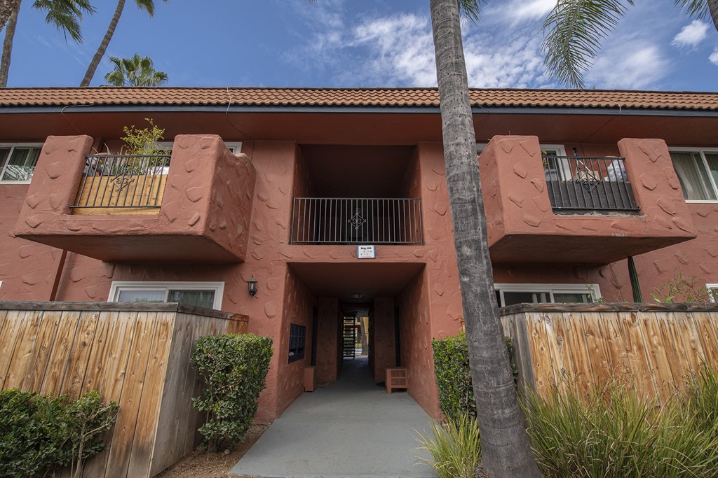 a red building with a tall palm tree in front of it at Villa Quixote Apartments, Escondido, CA