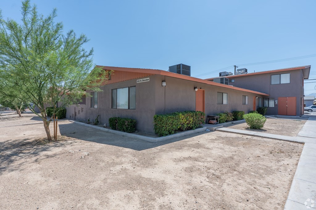 Apartment building with tree and sidewalk in front.