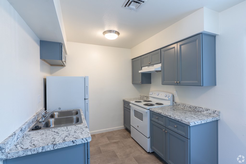 A kitchen with a white refrigerator, a white stove, and a marble countertop.