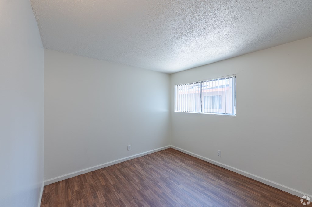 A bedroom with a window and wooden flooring.