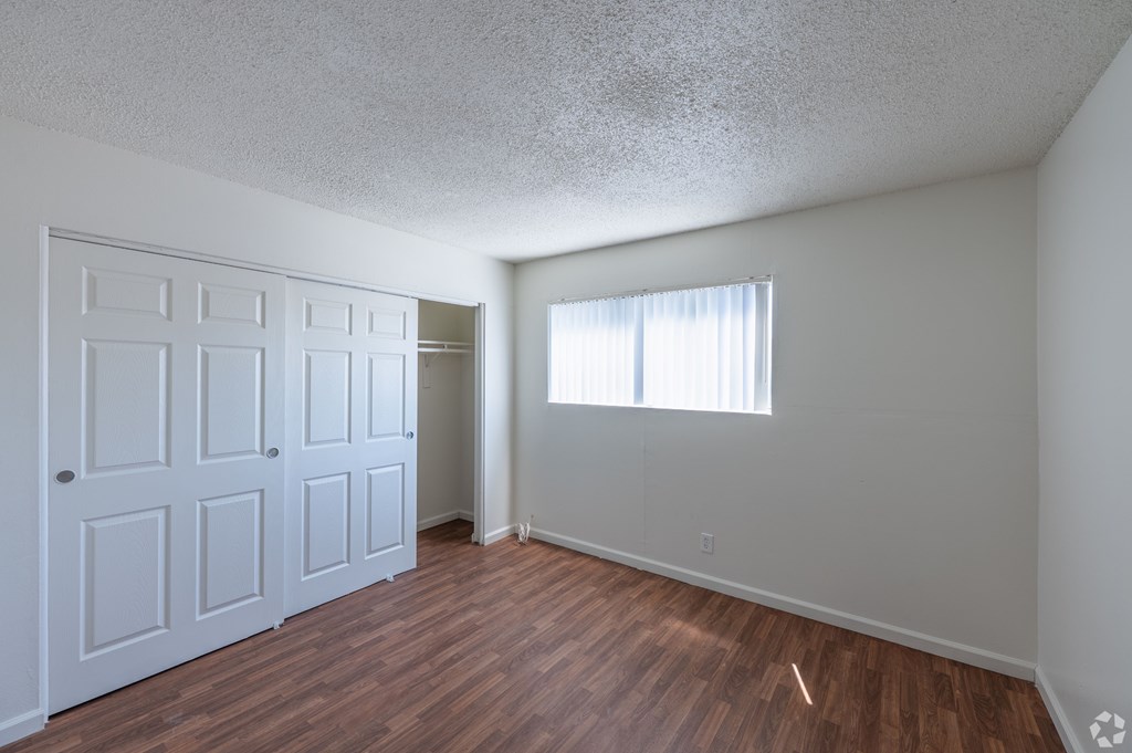 A bedroom with wooden flooring, a window, and a closet with sliding door.
