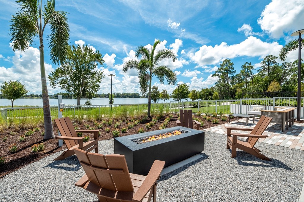 a patio with chairs and a fire pit and a lake in the background
