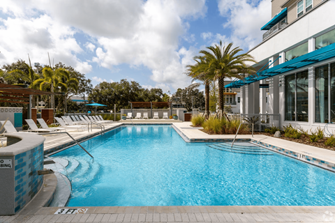 A large swimming pool with a blue tiled edge and a white building in the background.