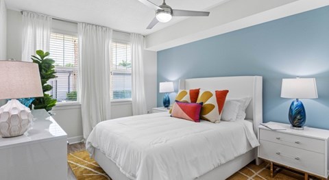 A bedroom with a white bed, a white nightstand, and a ceiling fan.