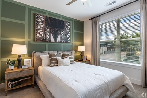 A bedroom with a large bed, a nightstand with a lamp, and a picture of a bridge on the wall.