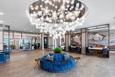 A large, modern chandelier hangs above a blue, round sofa in a spacious, well-lit room.