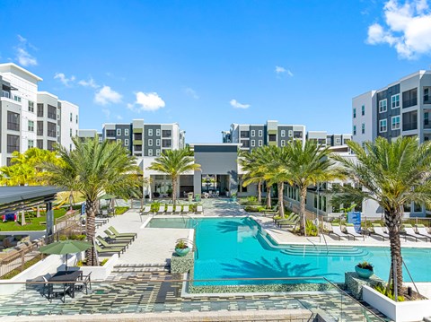 A pool surrounded by palm trees and a building in the background.