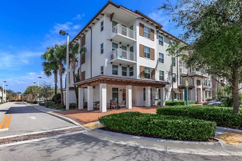 A white apartment building with a balcony and a tree in front.