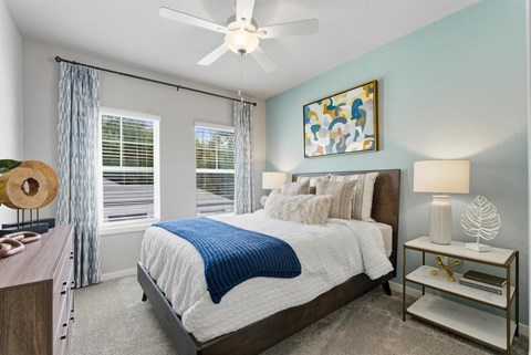 A bedroom with a bed, a ceiling fan, and a nightstand with a lamp.