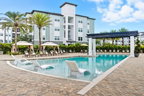 A swimming pool with sun loungers and a building in the background.
