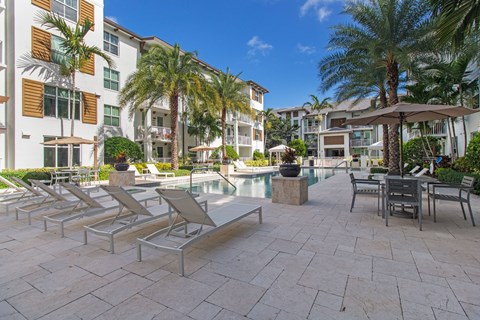 a swimming pool with lounge chairs and umbrellas in front of a building