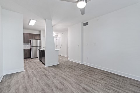 the living room and kitchen of an apartment with white walls and wood flooring