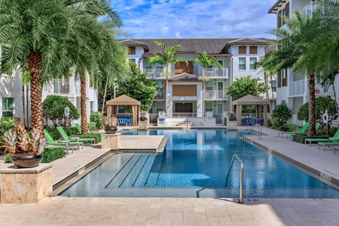 A large swimming pool surrounded by palm trees and lounge chairs.