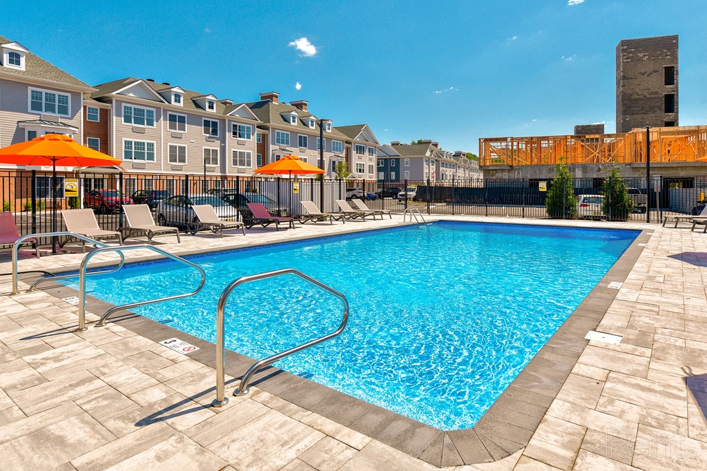 a swimming pool with chairs and umbrellas in front of apartment buildings at Solo at North Bergen, New Jersey