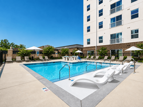 A large swimming pool with lounge chairs and umbrellas in front of a tall building.