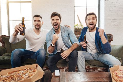 three men sitting on a couch with beer and a pizza