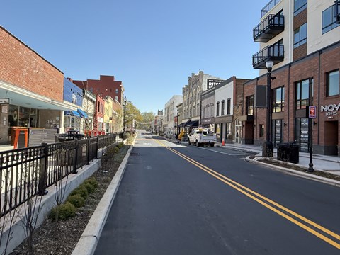 A city street with buildings on both sides and a truck driving down the road.