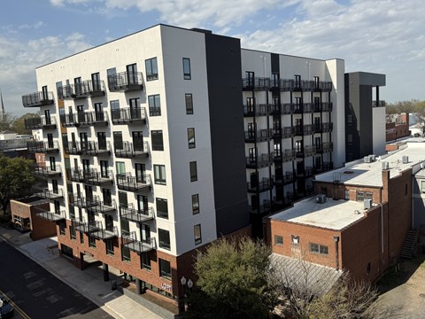 A modern apartment building with balconies and a brick building in the foreground.