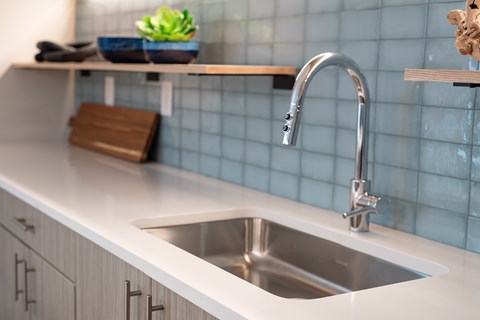 A modern kitchen with a white countertop and a stainless steel sink.