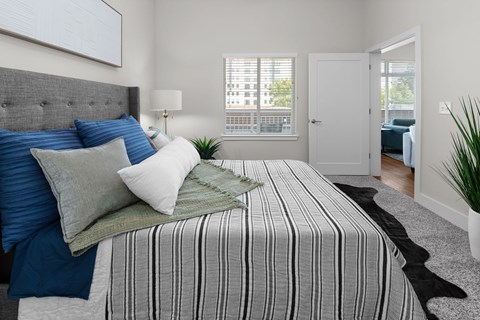 Bright primary bedroom featuring a plush bed, upholstered headboard, oversized windows, and contemporary finishes at NOVI Concord apartments.