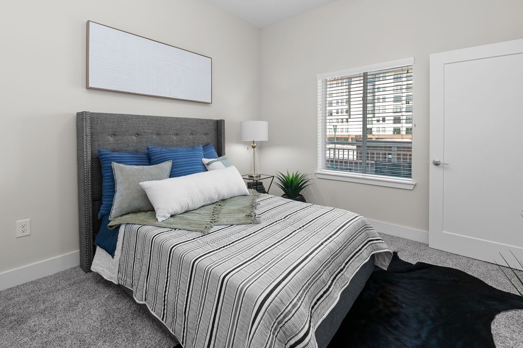 A bedroom with a bed, pillows, a lamp, and a window.