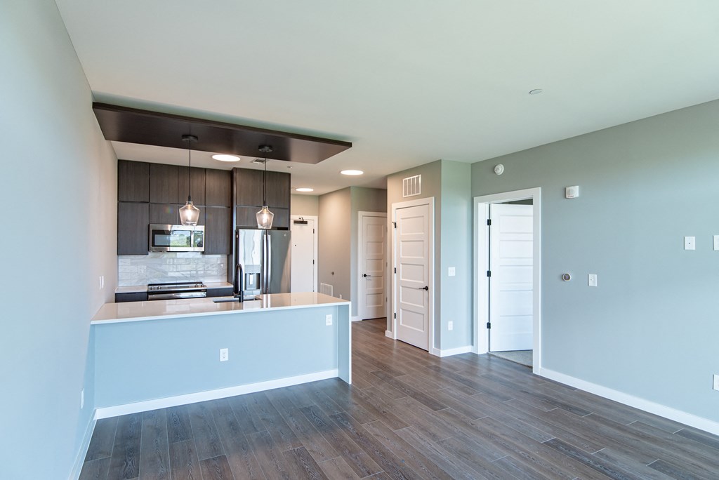 an empty living room with a kitchen and a door to a hallway